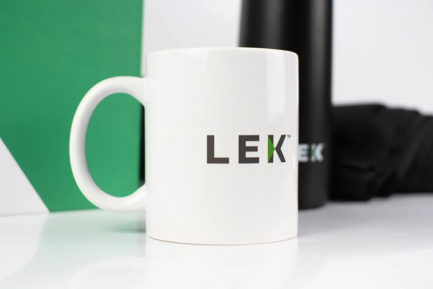 Caneca branca com logotipo impresso, ao lado de garrafa térmica preta do mesmo kit