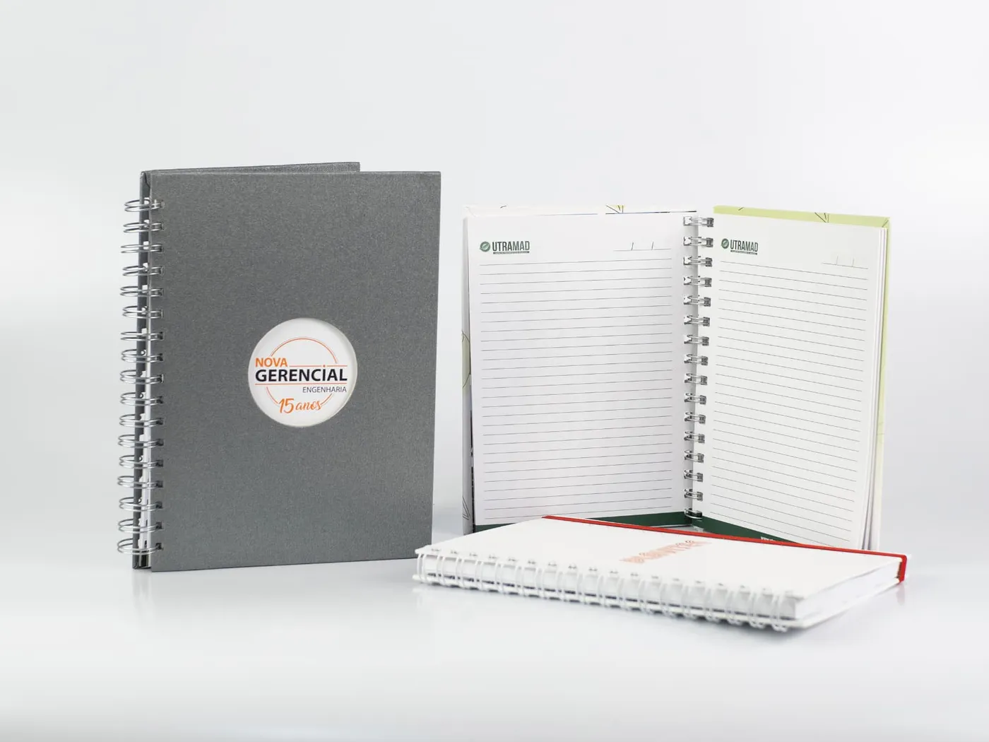 Caderno wire-o com capa em papel texturizado e janela recortada, ao lado de cadernos abertos