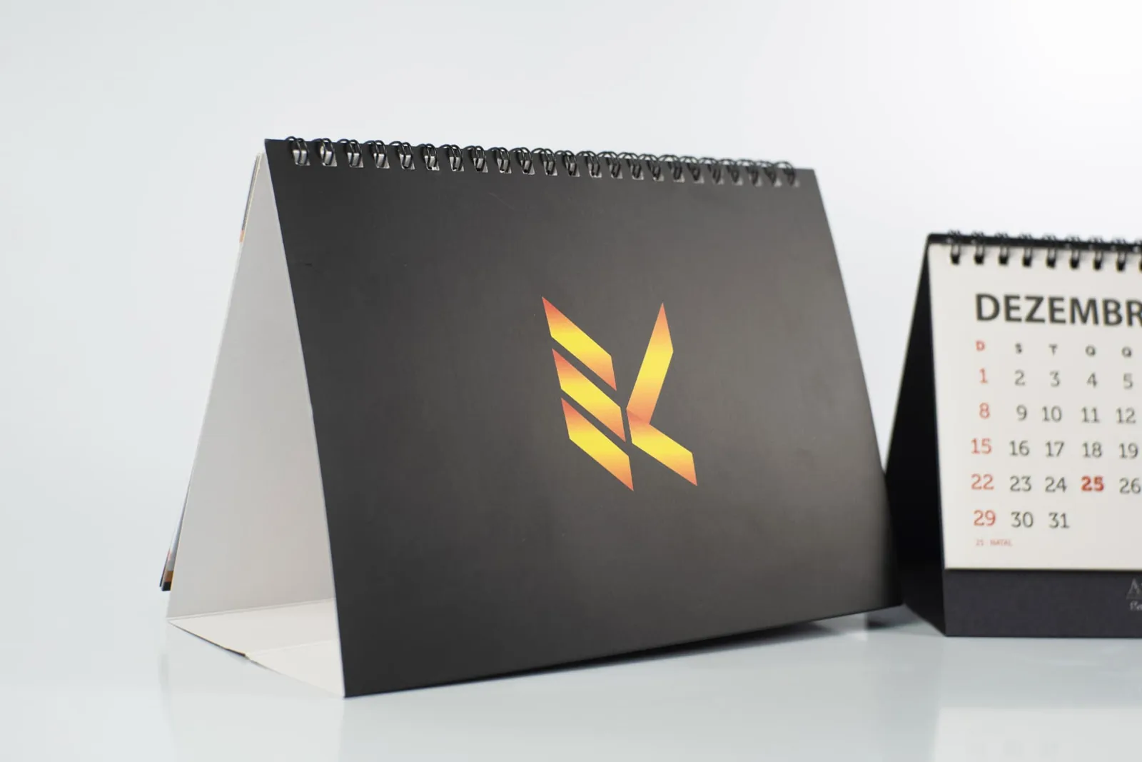Detalhe do calendário de mesa com capa preta e logotipo em degradê laranja