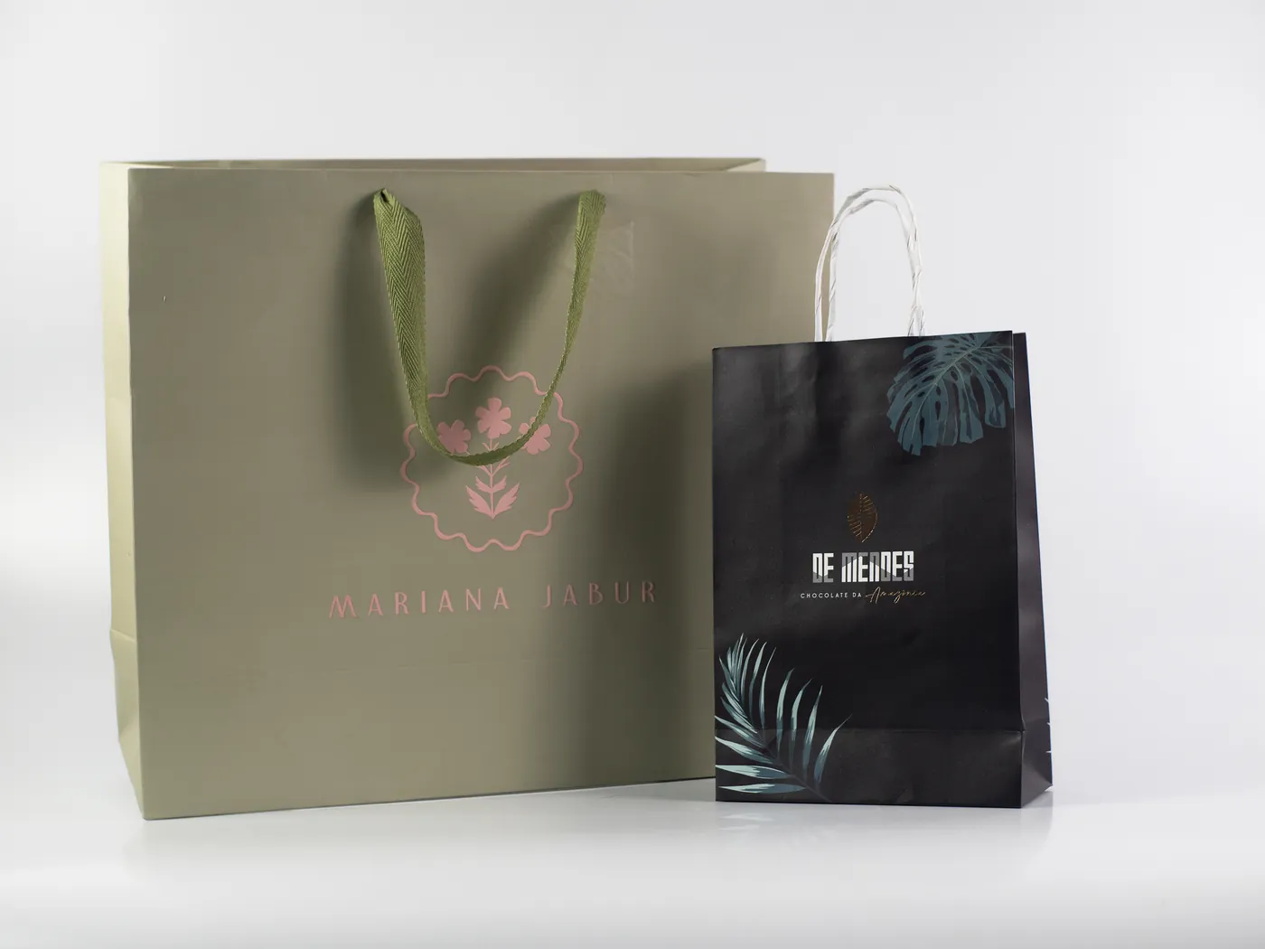 Sacolas personalizadas em papel fosco, uma verde com alça de fita e outra preta com hot stamping