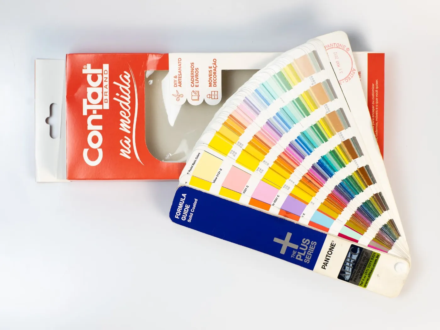 Embalagem Con-Tact com janela ao lado do leque Pantone Formula Guide