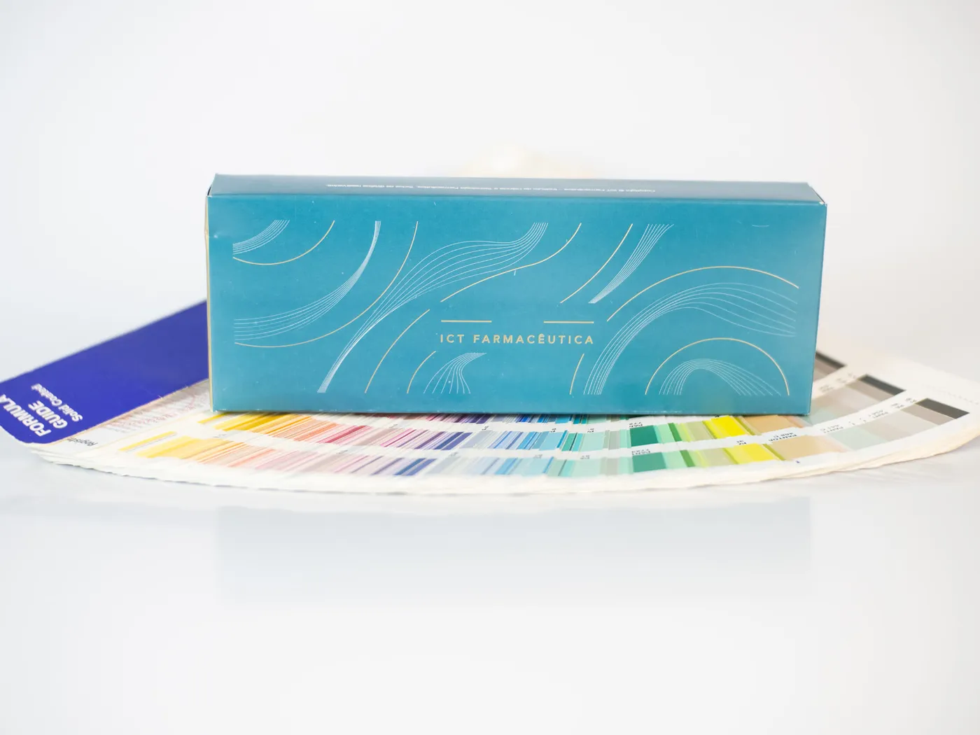 Caixa ICT Farmacêutica em verde-petróleo apoiada sobre o leque Pantone aberto